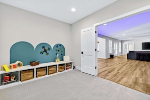 Un intérieur moderne avec une porte blanche, un espace de jeux avec des jouets et un salon doté d’un canapé foncé.