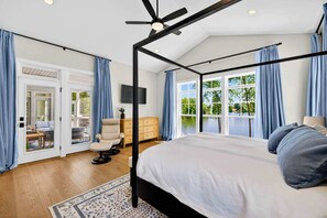 Un dormitorio con cama con dosel, ventilador de techo, televisor y vistas al exterior.