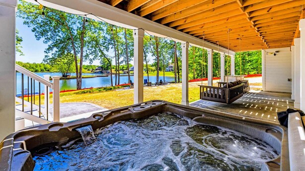 Et overdækket udendørs område med jacuzzi, træloft og udsigt til pool og grønt.