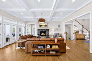 Ein großzügiger Wohnraum mit Kamin, Ledersofa, Couchtisch aus Holz und einer Treppe, die in eine weitere Ebene führt.