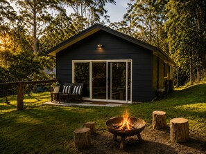 A dark-colored cabin with a fire pit, outdoor seating, and a sliding glass door.