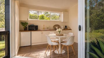 A modern kitchen with white cabinets, a dining table with white chairs, and a view of greenery outside.
