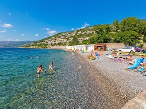 A pebble beach with clear water, people swimming, and beach chairs. - Miraval by Interhome (Sveti Juraj)