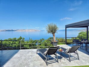 Eine Terrasse mit zwei Liegestühlen, einem Tisch mit Obst und Blick auf Meer und Berge.