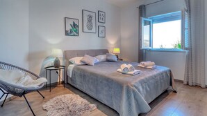 Een slaapkamer met een bed, twee bedlampen, een stoel, een vloerkleed en een raam met gordijnen.