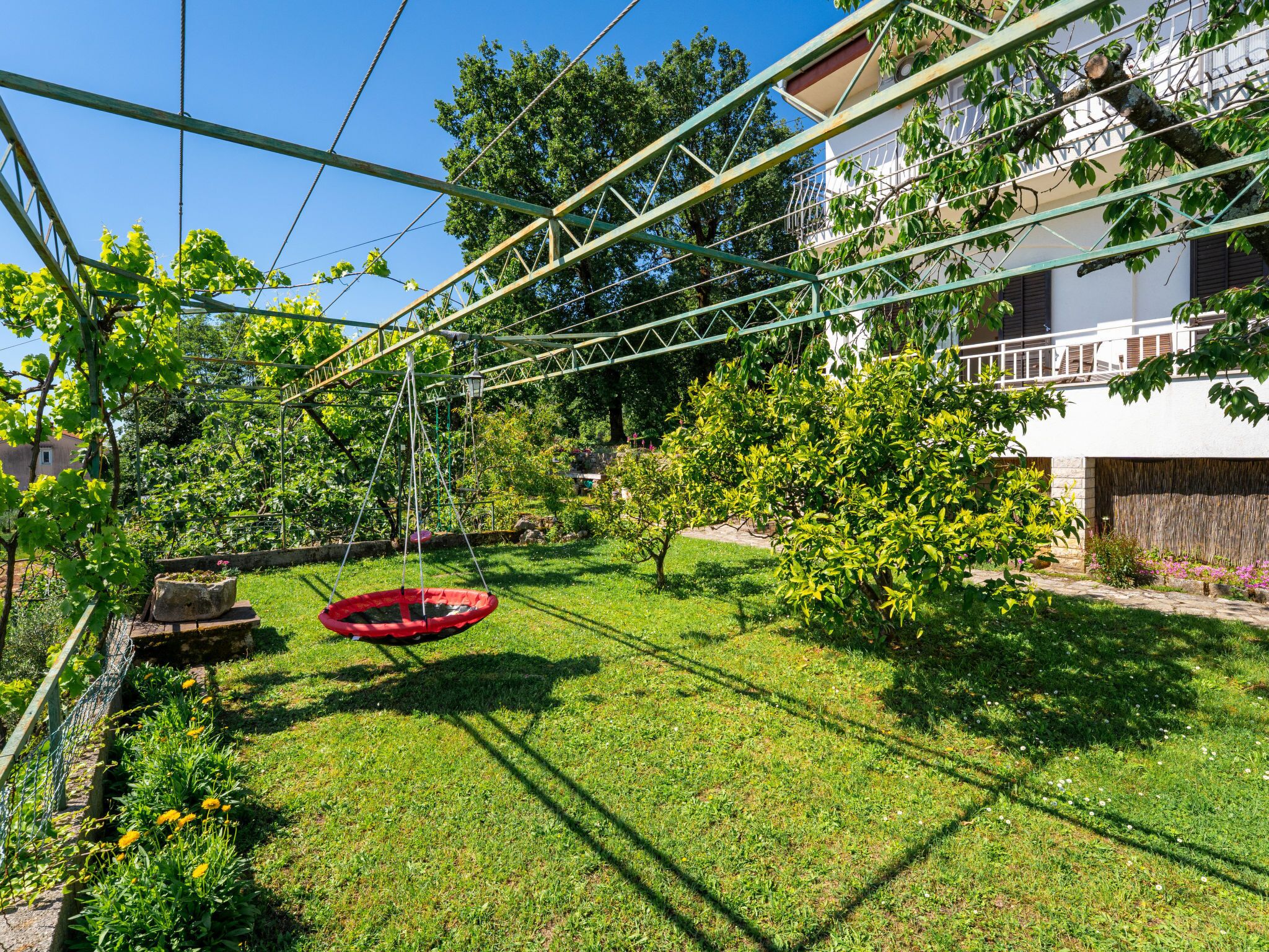 A backyard with a swing set, a red trampoline, and a garden with various plants.