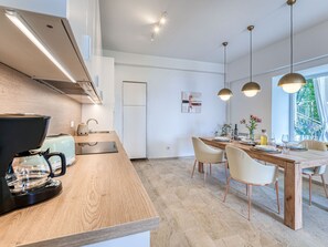 A modern kitchen with a coffee maker, a sink, and a dining area with a wooden table and chairs. - Apartment Emil by Interhome (Lovran)