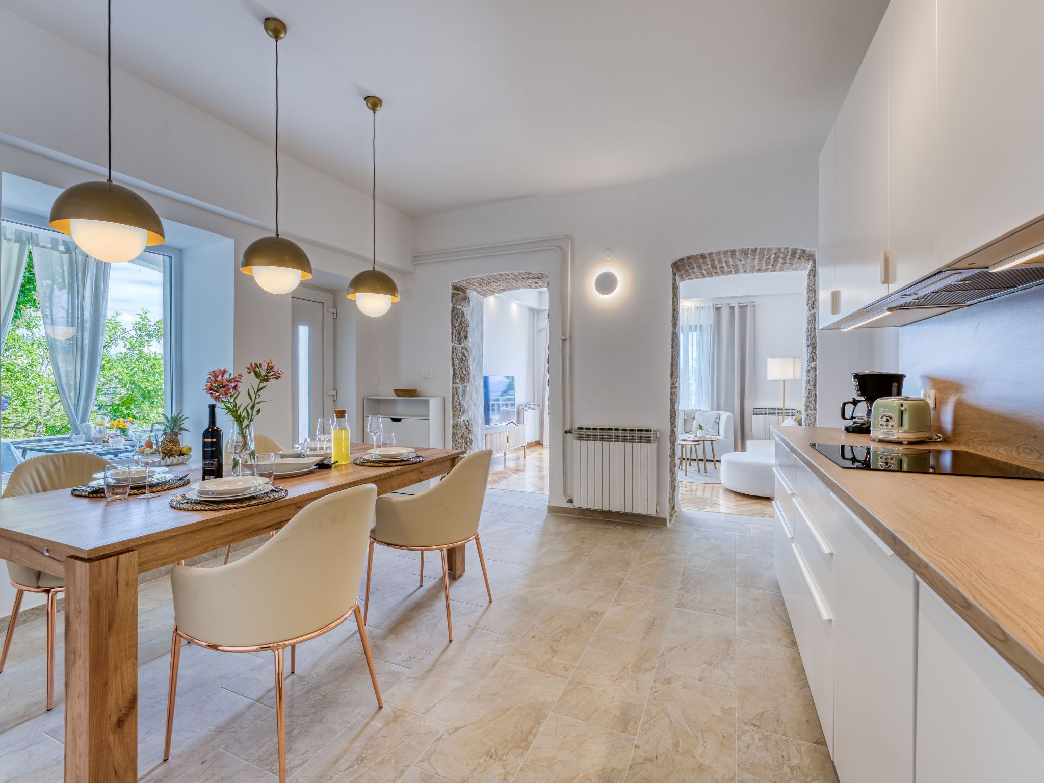 Une cuisine moderne avec un plan de travail en bois, un coin repas doté d’une longue table et de chaises, et un éclairage suspendu.