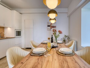 A modern kitchen with white cabinets, a wooden dining table set with plates, glasses, and a bottle. - Apartment Emil by Interhome (Lovran)