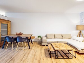 Ein modernes Wohnzimmer mit einem Holzesstisch, zwei blauen Stühlen, einem beigen Sofa und einem Couchtisch aus Holz.