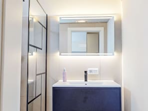A modern bathroom with a white sink, dark cabinet, and a mirror with integrated lighting. - Renovierte Erdgeschosswohnung by Interhome (Simmersfeld)