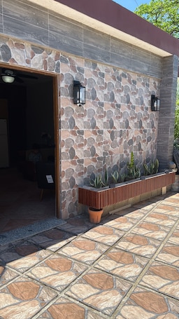 A stone exterior wall with a door, two wall-mounted lights, and a planter with plants.. Luxury apartment with a pool and hot water—offering comfort, and pets are welcom