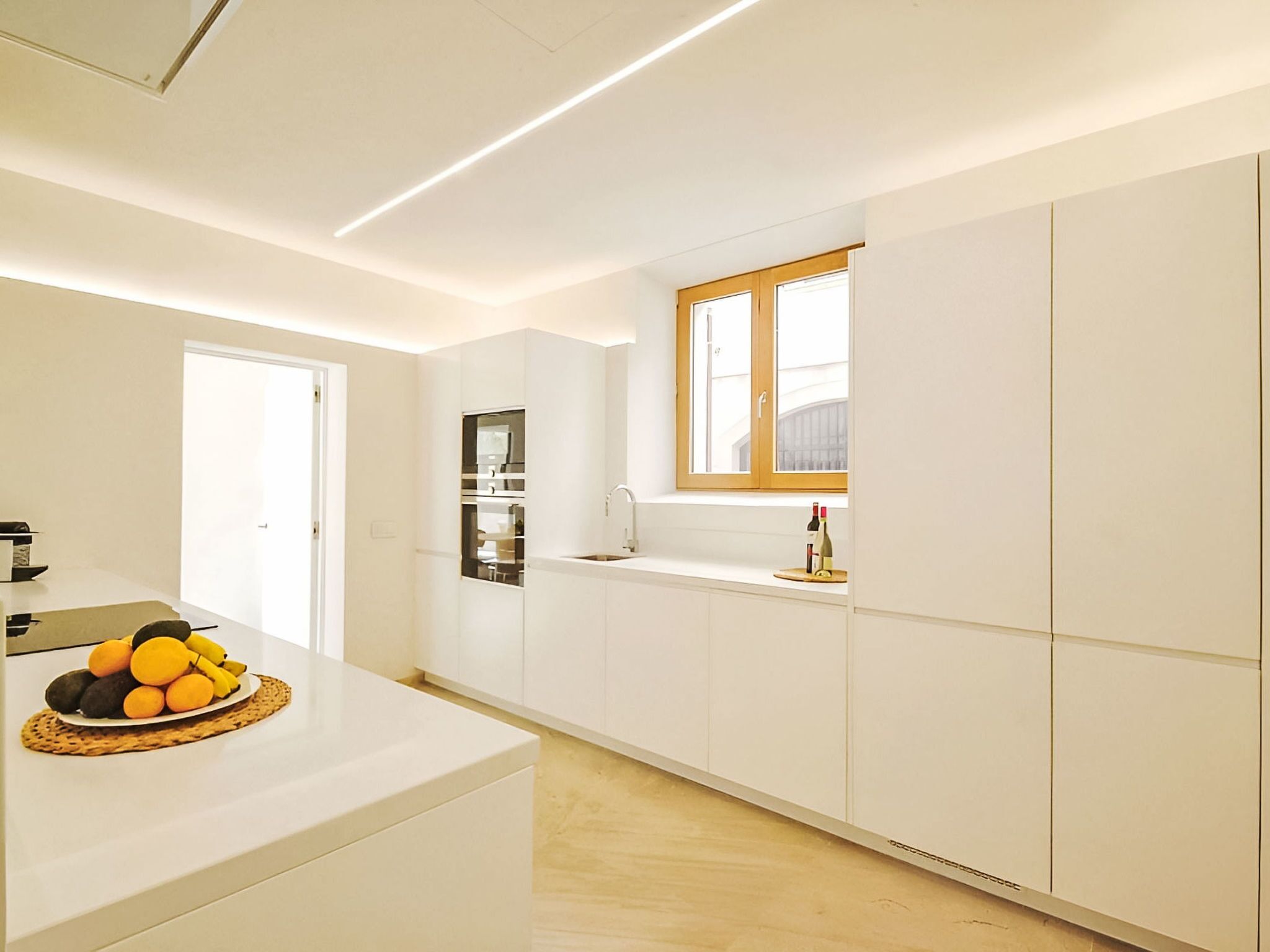 A modern kitchen with white cabinetry, a built-in oven, and a window with a view.