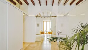 Ein modernes Interieur mit einem Flur, der in einen Essbereich führt, mit einer großen Topfpflanze, Holzbalken und einer Glastrennwand.