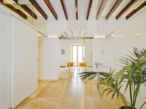 Ein modernes Interieur mit einem Flur, der in einen Essbereich führt, mit einer großen Topfpflanze, Holzbalken und einer Glastrennwand.