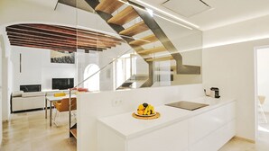 Eine moderne Küche mit Kochinsel, ein Essbereich mit Sofa und Stühlen sowie eine Treppe, die in eine obere Ebene führt.