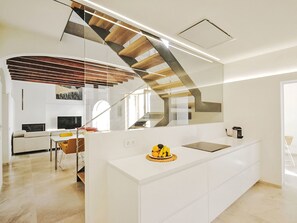 Eine moderne Küche mit Kochinsel, ein Essbereich mit Sofa und Stühlen sowie eine Treppe, die in eine obere Ebene führt.