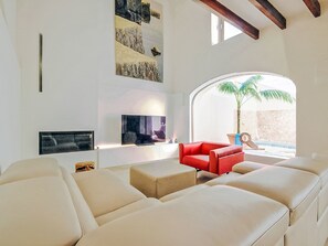 Ein modernes Wohnzimmer mit großem Fernseher, einem roten Sofa und Blick auf einen Pool.
