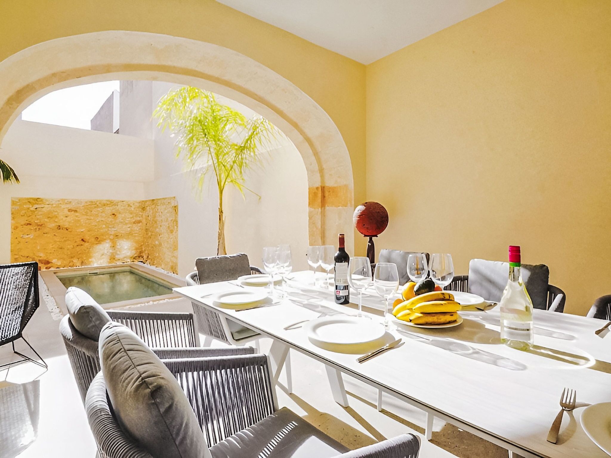A dining area with a long table, chairs, and a plant in the background.