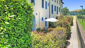 Ein Gebäude mit mehreren Fenstern, einem gepflasterten Weg und einem weißen Sonnenschirm.