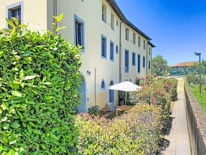 Ein Gebäude mit mehreren Fenstern, einem gepflasterten Weg und einem weißen Sonnenschirm.