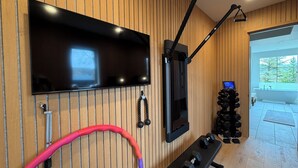 Habitación con una televisión montada en la pared, una barra de dominadas, un juego de mancuernas y vistas al exterior.