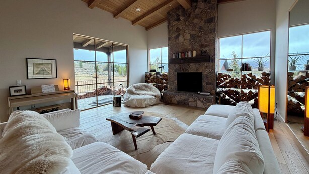 Un salón amplio con chimenea de piedra, ventanas grandes y un techo alto de madera.