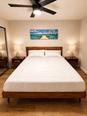 A bedroom with a bed, a ceiling fan, a painting, and two bedside lamps.