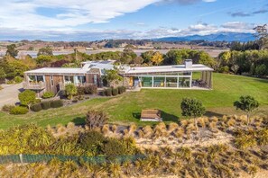 Una casa moderna con un amplio ventanal, rodeada de un césped cuidado y diversos arbustos.