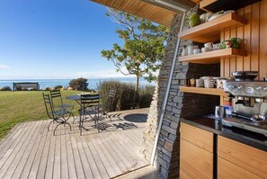 En udendørs terrasse med et bord og stole, en stenvæg og havudsigt.