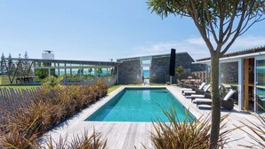 A modern pool area with a clear view of the ocean, a wooden deck, and lounge chairs. - Kina Retreat - Main House with Pool Access (Kina Peninsula)