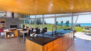 A modern kitchen with a large island, wooden cabinetry, and a view of the sea. - Kina Retreat - Main House with Pool Access (Kina Peninsula)
