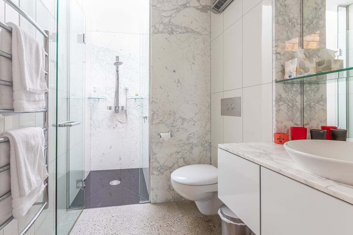 Une salle de bain moderne avec une douche à parois de verre, des toilettes blanches et un comptoir en marbre.