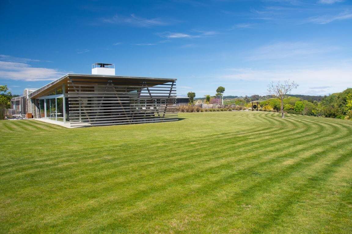 A modern building with a sloped roof and a covered outdoor area, surrounded by a well-maintained lawn.