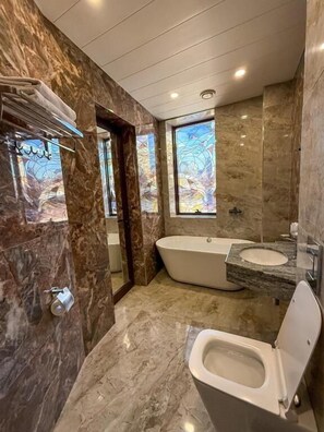 A bathroom with a bathtub, toilet, and sink, marble walls, and a window with a stained glass design. - Israel Ori Hotel (Yerevan)