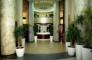 A lobby with a reception desk, large columns, potted plants, and a circular ceiling design. - Israel Ori Hotel (Yerevan)