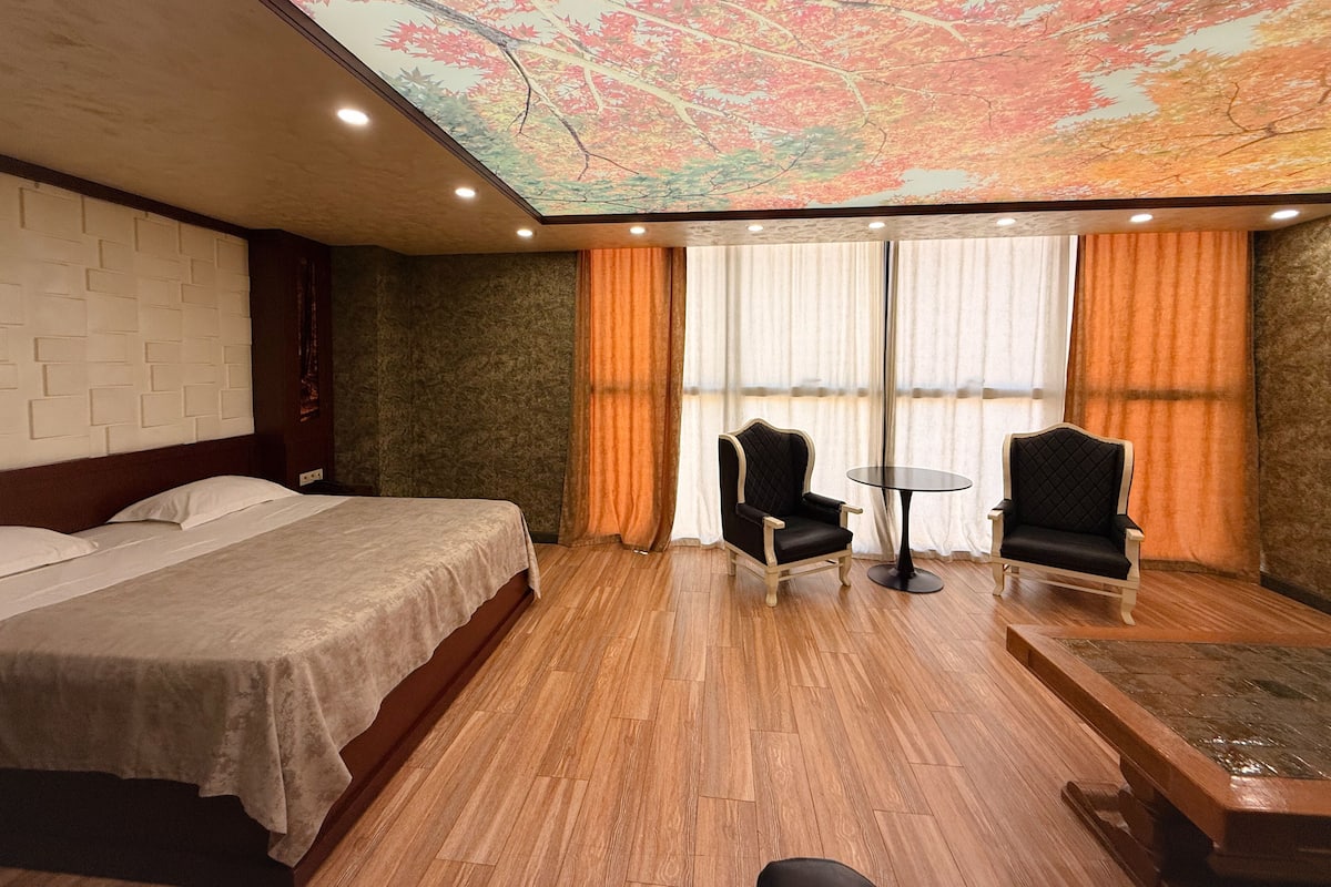 A hotel room with a bed, two armchairs, a small table, and a ceiling mural.