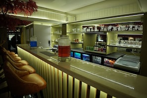 A bar area with a counter, stools, shelves with glassware, and a refrigerated display.