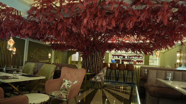 A restaurant with a high ceiling, hanging red foliage, and a bar area with stools. - Trevon Twin Tree Inn (Dhanbad)
