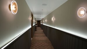 A hallway with patterned carpet, wall-mounted lights, and a wooden panel design. - Trevon Twin Tree Inn (Dhanbad)