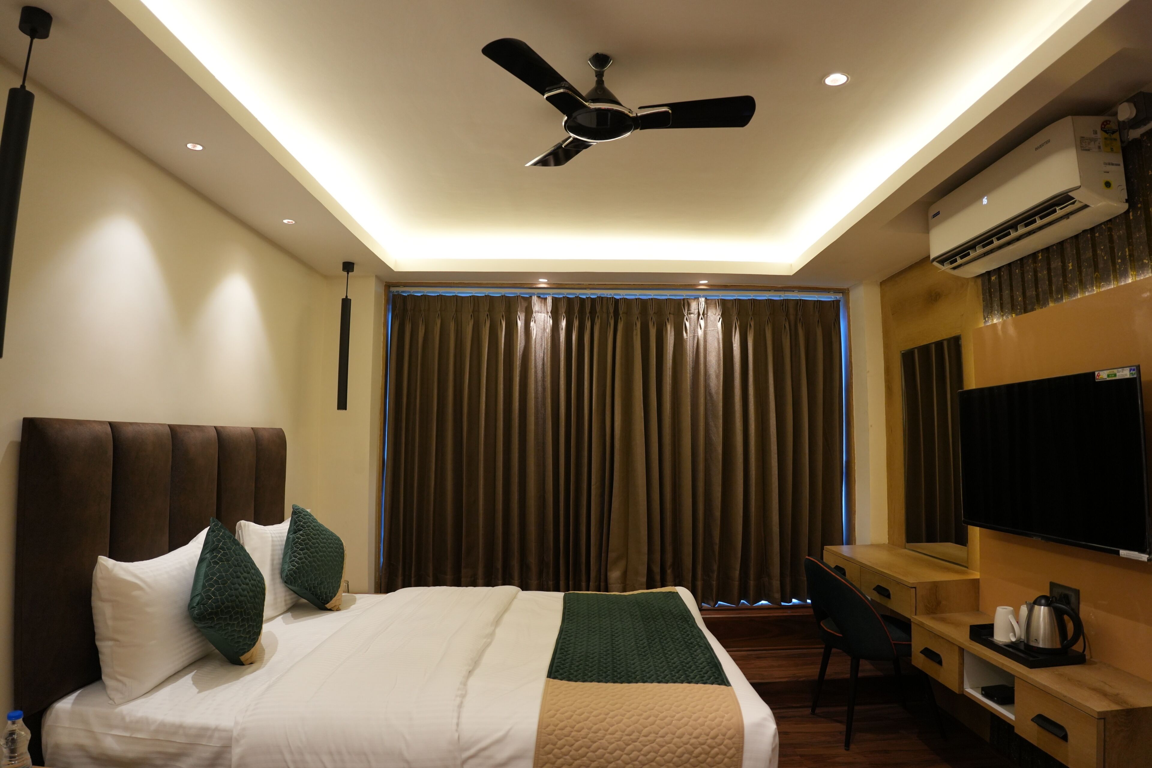 A hotel room with a bed, a desk, a television, and an air conditioning unit.