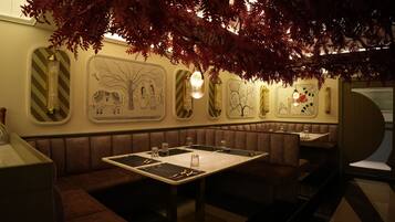 Un restaurante con cabinas y mesas, detalles decorativos en las paredes y lámparas colgantes.