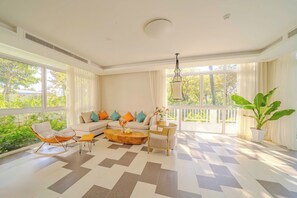 A spacious living room with a large window, a sofa set, a coffee table, and a potted plant. - Terra Garden Pool Village (Ngu Hanh Son)