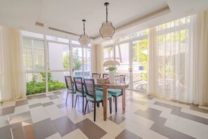 A dining area with a checkered floor, a round table, four chairs, two hanging pendant lights, and large windows with sheer curtains. - Terra Garden Pool Village (Ngu Hanh Son)