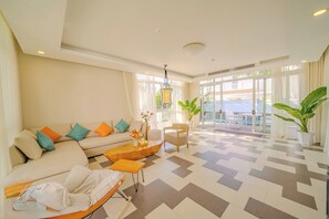 A modern hotel lobby with a sofa, armchairs, a coffee table, and a view of the sea through large windows. - Terra Garden Pool Village (Ngu Hanh Son)