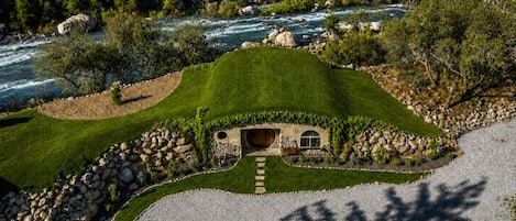 A house with a unique curved roof, surrounded by a well-maintained lawn and a river.