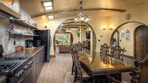 Uma cozinha ampla com uma ilha grande, armários de madeira e uma área de jantar com mesa de vidro e cadeiras ornamentadas.