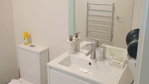 Un baño con inodoro, lavabo, espejo, toallero y secador de pelo.