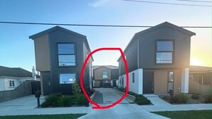 Una calle residencial moderna con casas de dos pisos, cielo despejado y acera.