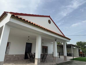 A white building with a red roof, a covered patio with chairs, and a black door. - Rural lodging los pozos 40 minutes from sevilla (Urbanización Santa Elo)